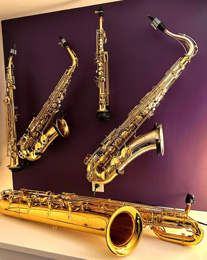 Five saxophones — two altos, a soprano, a tenor and a baritone — hanging on a deep plum wall